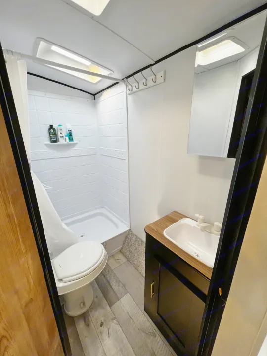 A well-lit, efficient RV rental bathroom featuring a shower, toilet, and modern sink vanity.. Keystone RV Springdale 2022