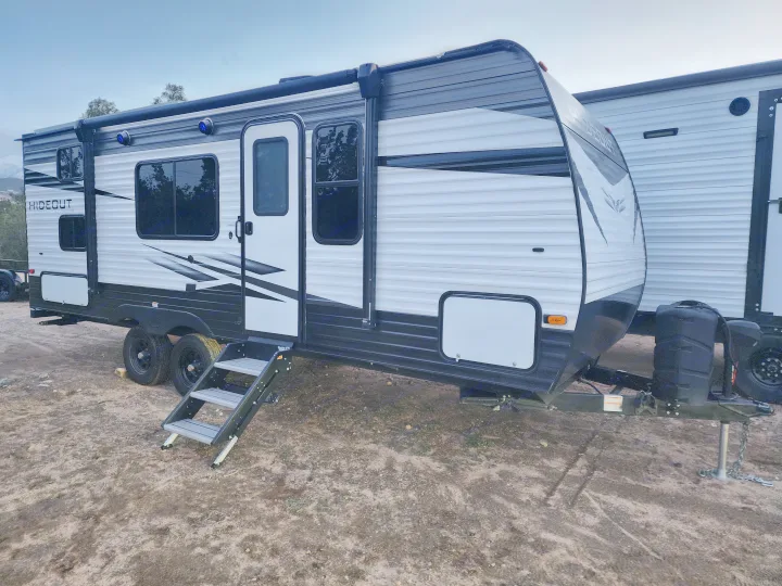 Modern white and black RV rental (travel trailer) with steps, parked on dirt, ready for adventure.. Keystone RV Hideout 2022