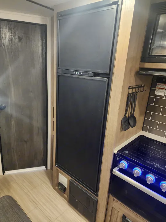 This RV rental kitchen features a modern setup with a fridge, microwave, and a Furrion stove with illuminated control knobs.. Keystone RV Hideout 2022