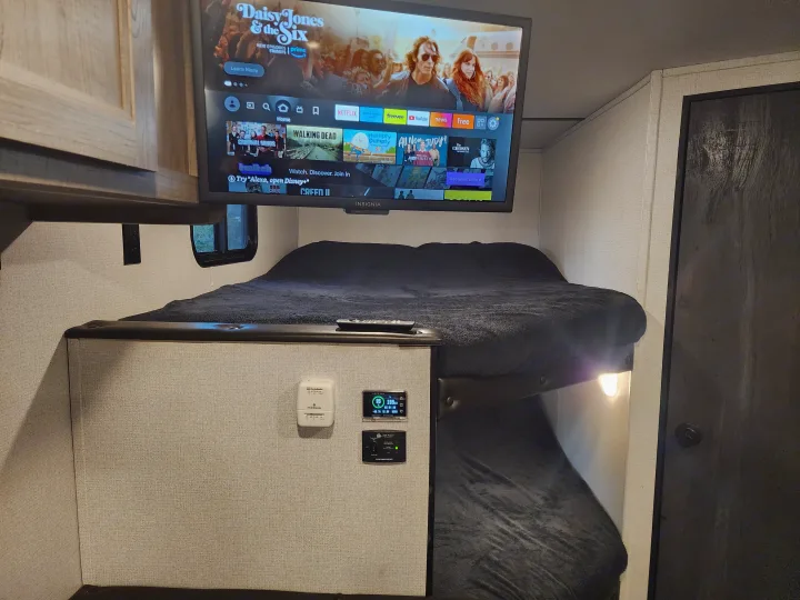 Cozy RV rental interior with bunk beds, a smart TV displaying streaming apps, a thermostat, and battery monitor.. Keystone RV Hideout 2022