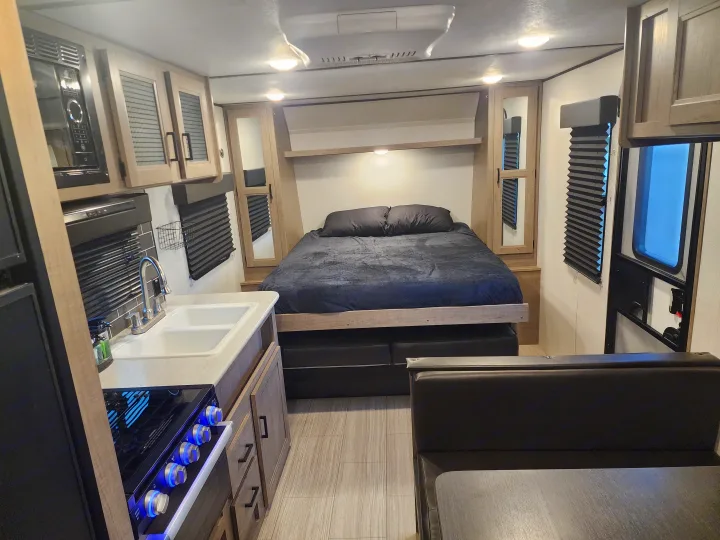 Modern rv rental interior: cozy bedroom, kitchen (microwave, sink, stove), and dining space.. Keystone RV Hideout 2022