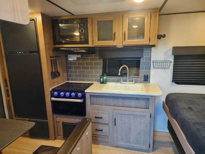 This RV rental features a well-equipped RV kitchen with a fridge, microwave, stove, sink, and an adjacent sleeping area.. Keystone RV Hideout 2022