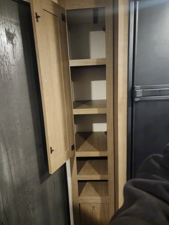 RV rental interior: Light wood storage cabinet with open cubbies and lower door, above dark wood-look floor.. Keystone RV Hideout 2022