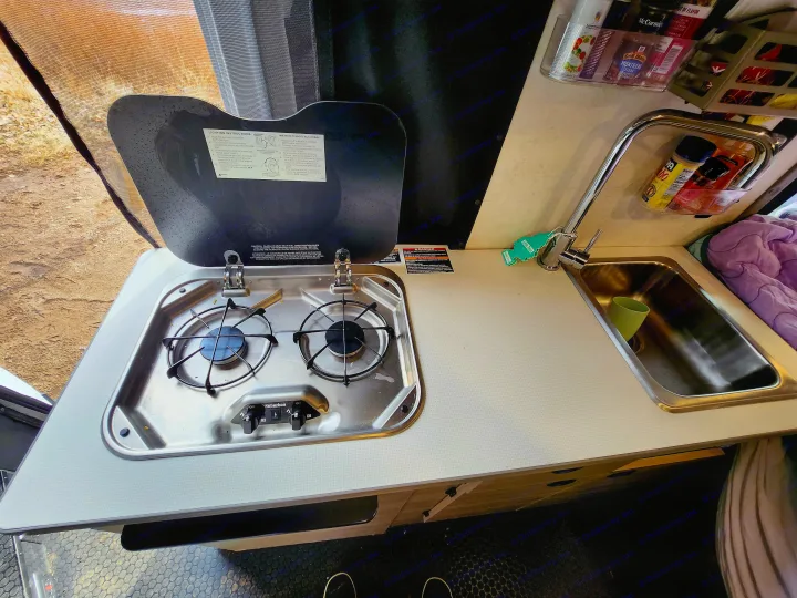 Compact RV rental kitchen featuring a Suburban stove, sink, and organized spices for travel cooking.. Winnebago Solis 2023