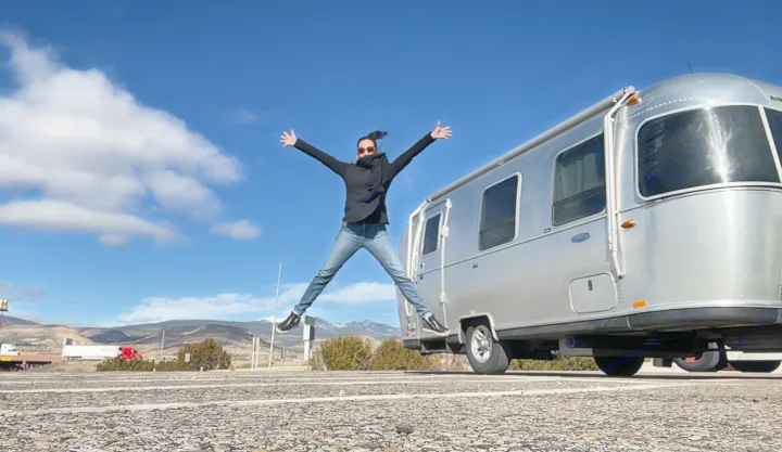 Joyful person jumps beside a sleek Airstream RV rental in a scenic mountain setting. Perfect for road trip adventures!. Airstream Sport 2019