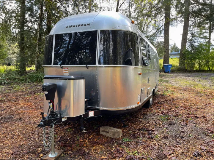 A sleek silver Airstream travel trailer, an excellent rv rental option, nestled in a serene woodland setting.. Airstream Sport 2019
