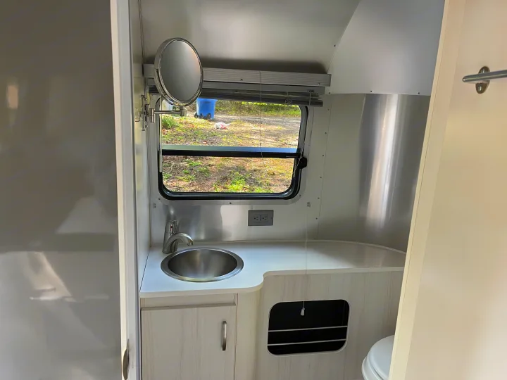 RV rental: interior view of a compact bathroom vanity with sink, mirror, window, and toilet.. Airstream Sport 2019