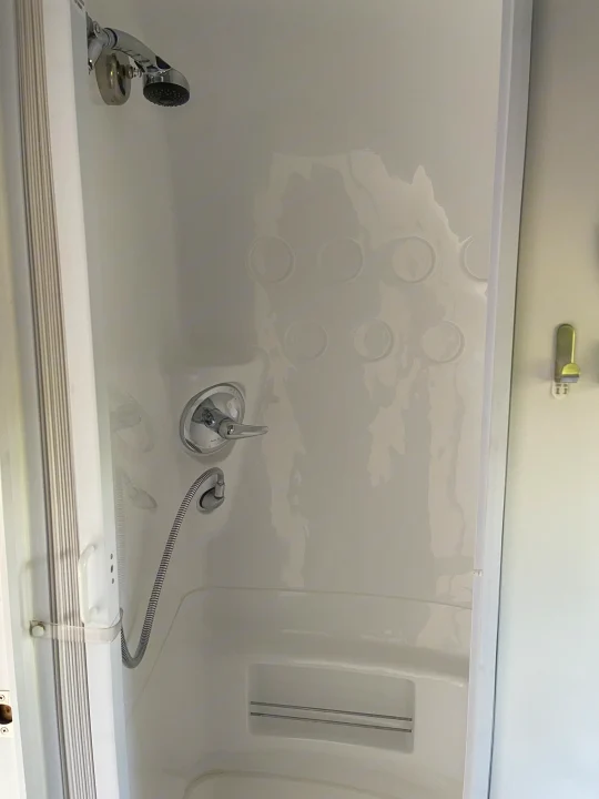 Clean white shower in an RV rental, featuring both fixed and handheld showerheads, a faucet, and a built-in storage shelf.. Airstream Sport 2019