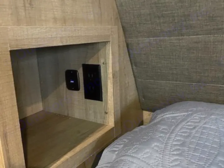 RV rental convenience: Built-in shelf with power outlets & USB charging in a cozy bedroom. Grey headboard and bed visible.. Grand Design Imagine 2022