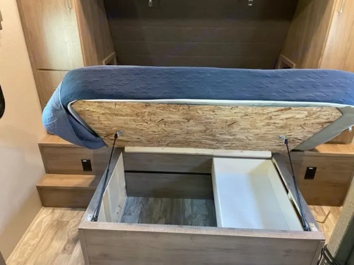 RV rental: A raised bed base reveals deep under-bed storage with support struts, ideal for maximizing space in an RV.. Grand Design Imagine 2022