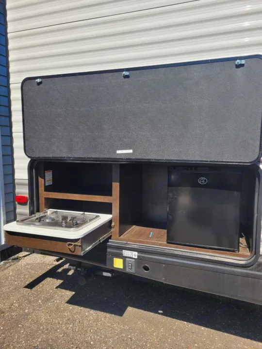 This rv rental's outdoor kitchen includes a pull-out stove, mini-fridge, and storage shelves, perfect for camping.. Heartland RVs Pioneer 2020
