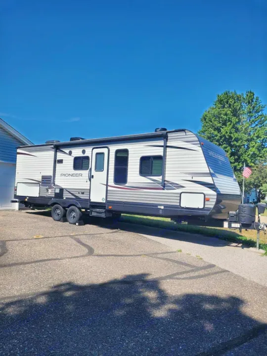 A large grey and white Pioneer travel trailer, an excellent RV rental option, parked on a paved driveway under a blue sky.. Heartland RVs Pioneer 2020
