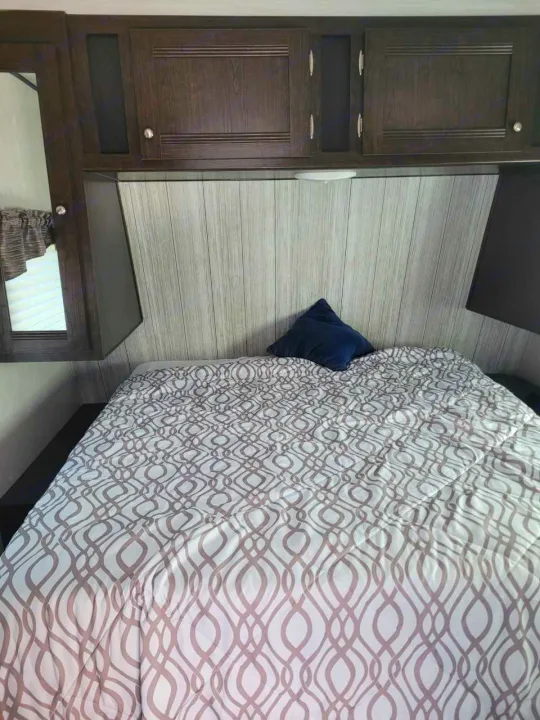 Cozy RV rental bedroom with patterned bedspread, overhead cabinets, and built-in mirror.. Heartland RVs Pioneer 2020