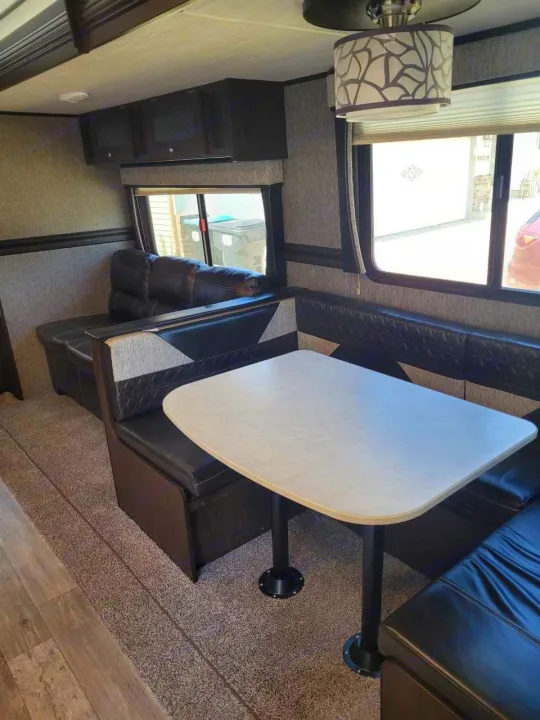 Comfortable RV rental interior showing a dinette with black upholstery, table, and lounge sofa.. Heartland RVs Pioneer 2020