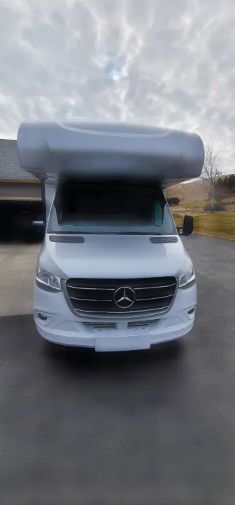 Front view of a white Mercedes-Benz Sprinter RV rental, a Forest River camper van with a grey top, parked on asphalt.. Forest River Forester 2401B 2023