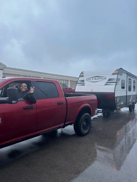 A happy woman flashes peace signs from her red truck, hitched to an Olympia RV rental for a trip.. Highland Ridge RV Olympia 2022