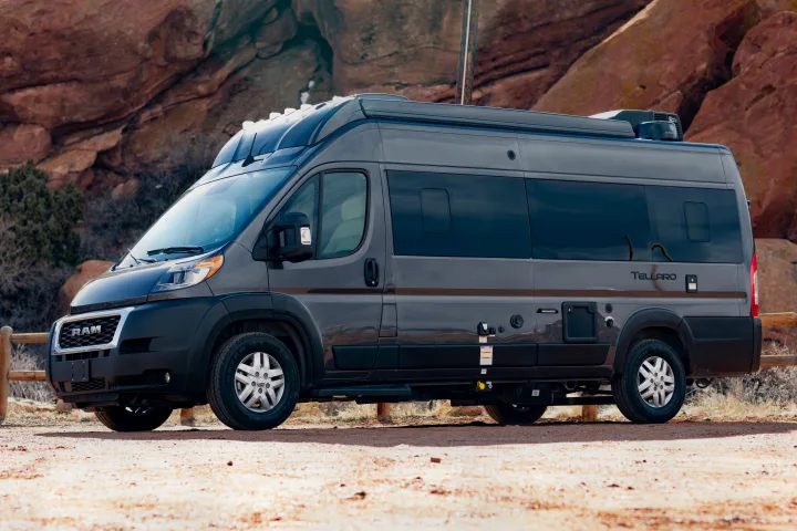A dark gray camper van sits on a dirt road with red rock formations in the background. Ideal for an RV rental adventure.. Thor Tellaro 2023