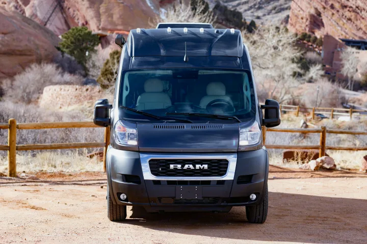 Front view of a black Ram ProMaster RV rental, parked on a dirt path with a rocky landscape behind it.. Thor Tellaro 2023
