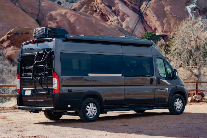 Dark grey Tellaro RV rental camper van with a bike rack, parked amidst scenic red rock formations.. Thor Tellaro 2023