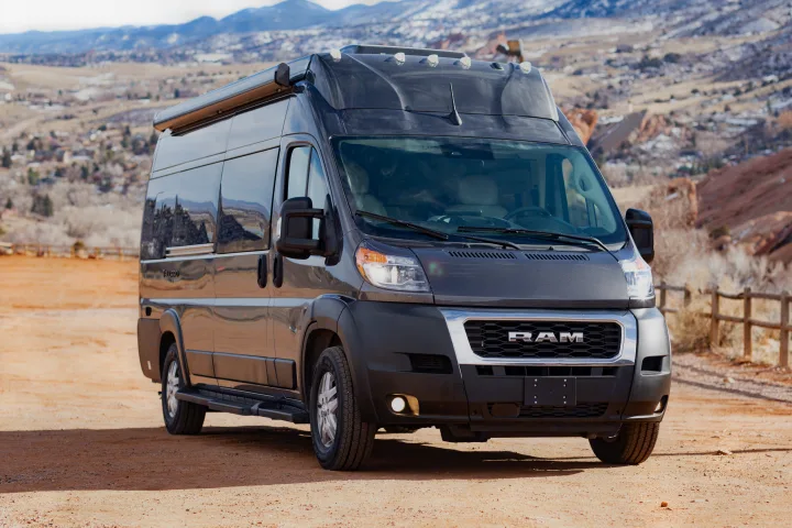 Dark gray RAM ProMaster camper van for rv rental parked on a dirt road, with mountains and red rock formations visible.. Thor Tellaro 2023