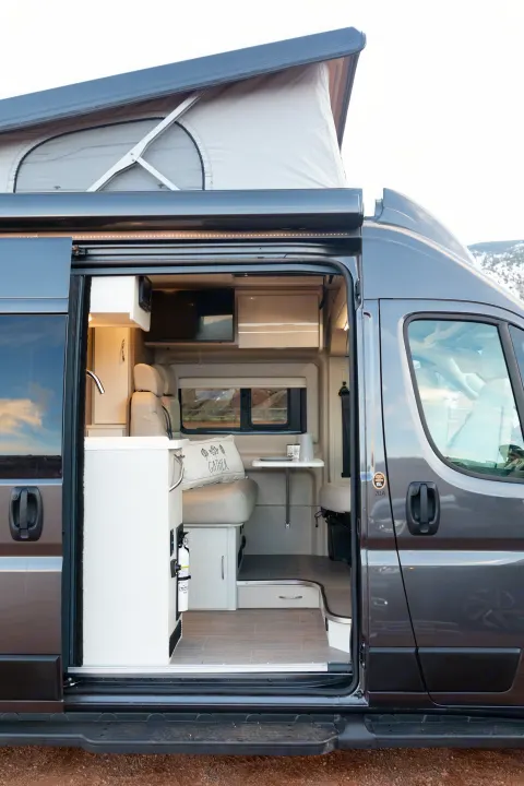 Spacious gray pop-top camper van for rv rental, showing comfy interior with kitchen, seating, and expandable roof for adventure.. Thor Tellaro 2023