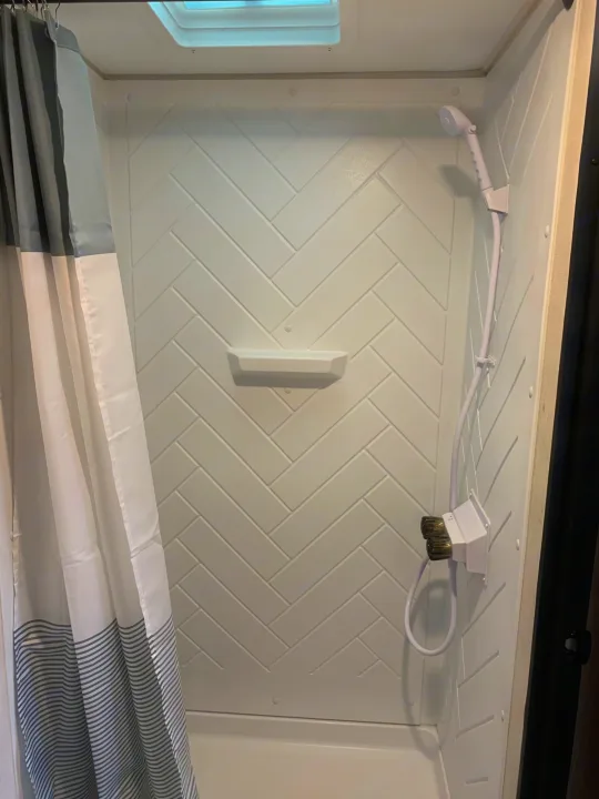 RV rental shower interior with white patterned walls, handheld shower, and skylight. Clean and compact design.. Avenger LT 2022