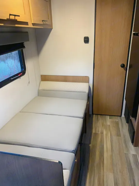 RV rental interior: window, light wood cabinets, convertible dinette bed, wood-look floor, and door with thermostat.. Avenger LT 2022
