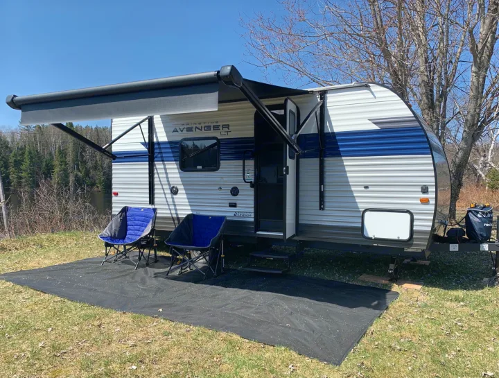 Scenic rv rental, a Prime Time Avenger LT, parked by water. Awning extended with chairs, perfect for outdoor camping.. Avenger LT 2022