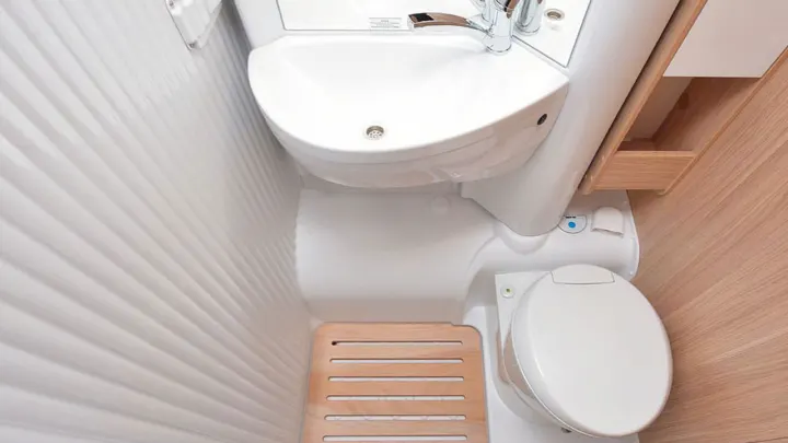 Compact RV rental wet bath featuring a corner sink, toilet, and wooden shower mat, ideal for small spaces.. Sunlight A72 2023
