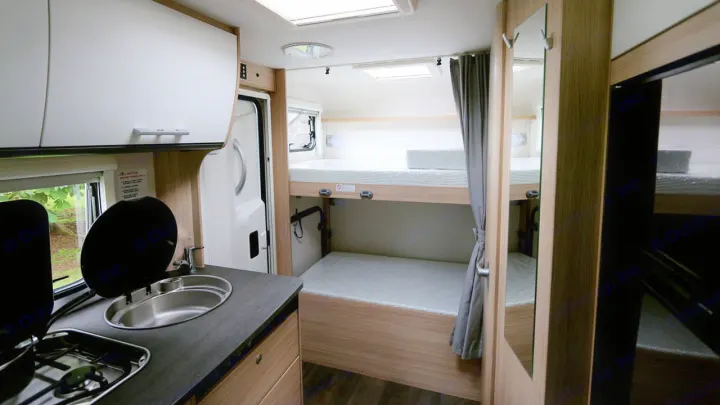 Inside an RV rental: Compact kitchen with sink & stove, plus comfortable bunk beds for travel convenience.. Sunlight A72 2023