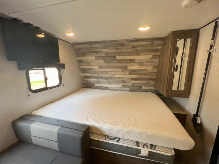 Cozy rv rental bedroom features a comfortable bed, mounted TV, and stylish wood-paneled wall, perfect for travel.. Crossroads Zinger Lite 2022