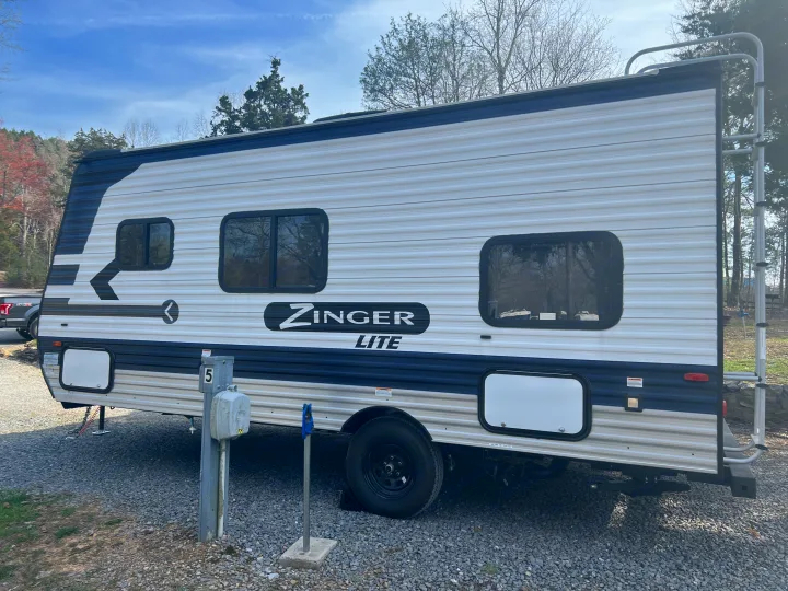 A blue/white Zinger Lite RV rental travel trailer is parked on a gravel campsite, ideal for outdoor adventures.. Crossroads Zinger Lite 2022