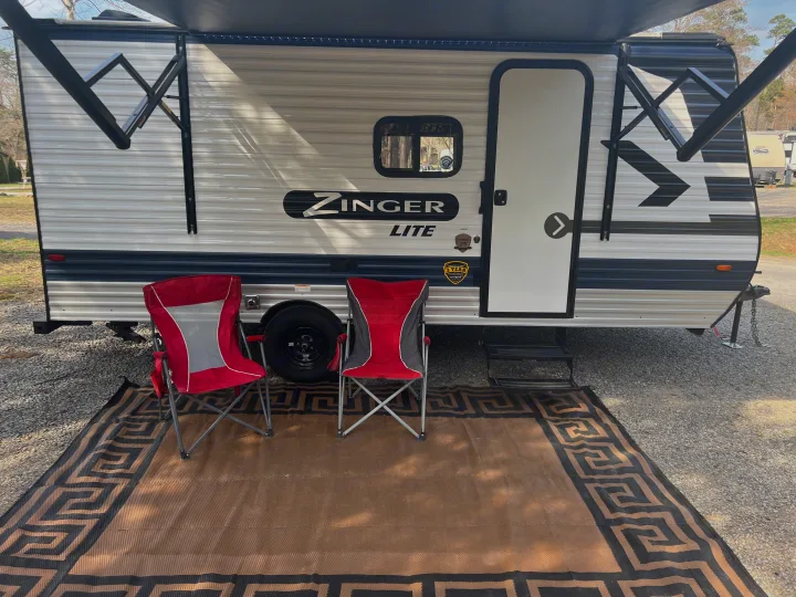 This Zinger Lite RV rental setup includes an awning, two red chairs, and an outdoor rug for campsite comfort.. Crossroads Zinger Lite 2022