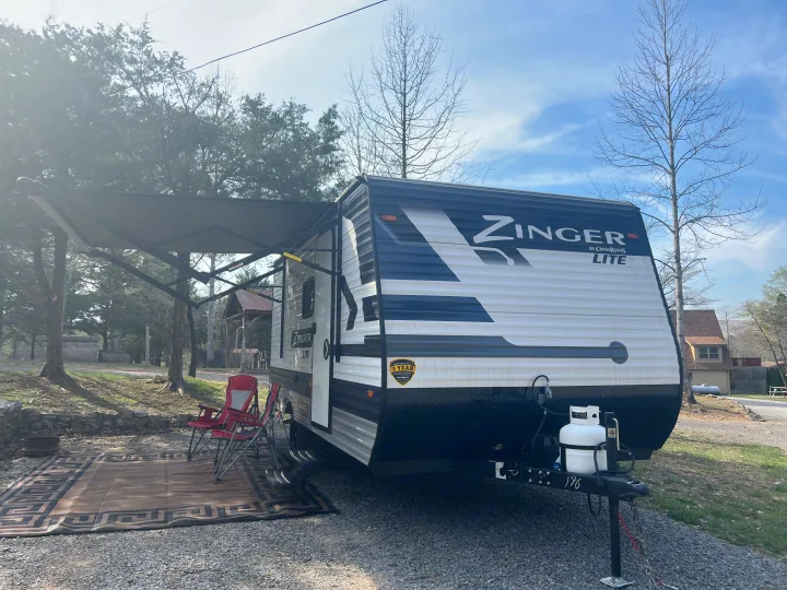 Enjoying the outdoors with an RV rental. This Zinger Lite travel trailer is set up with an awning and chairs at a peaceful campsite.. Crossroads Zinger Lite 2022