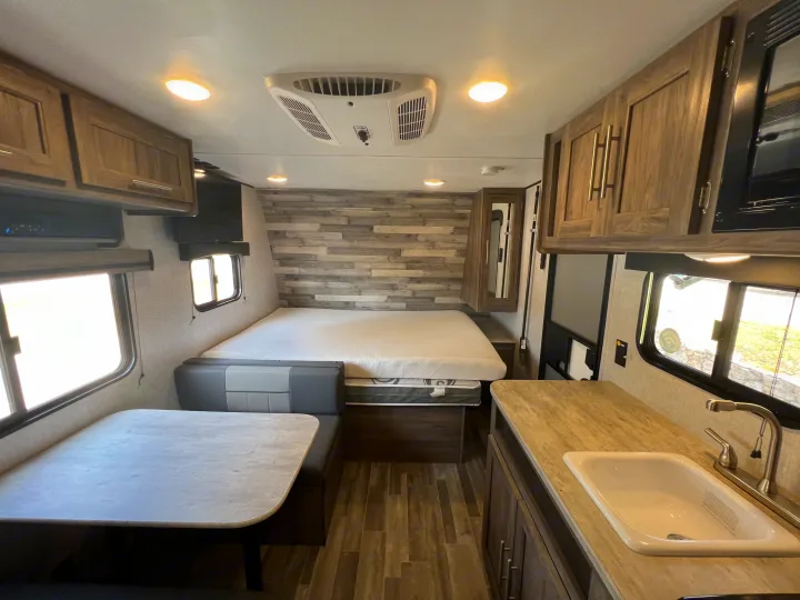 Spacious RV rental interior with a cozy bed, modern dinette, full kitchenette, and ample overhead cabinets.. Crossroads Zinger Lite 2022