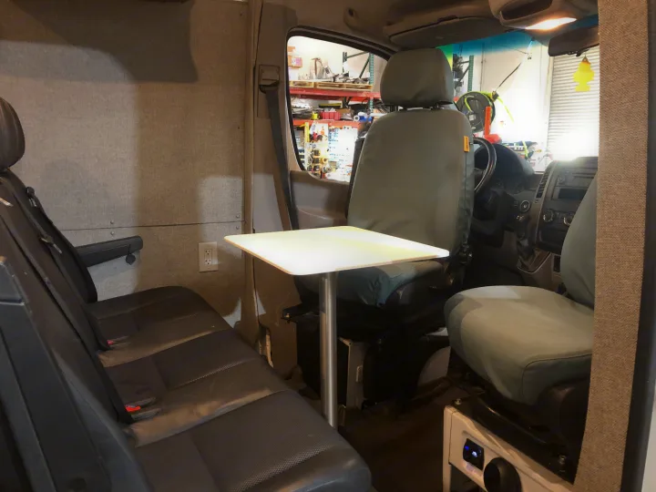 This RV rental interior features rear bench seating, a central table, and an electrical outlet, looking towards the front cabin.. Freightliner Sprinter 2012
