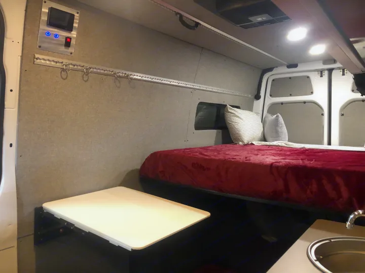 Inside this RV rental: a cozy bed, control panel, fold-down table, and small sink for compact living.. Freightliner Sprinter 2012