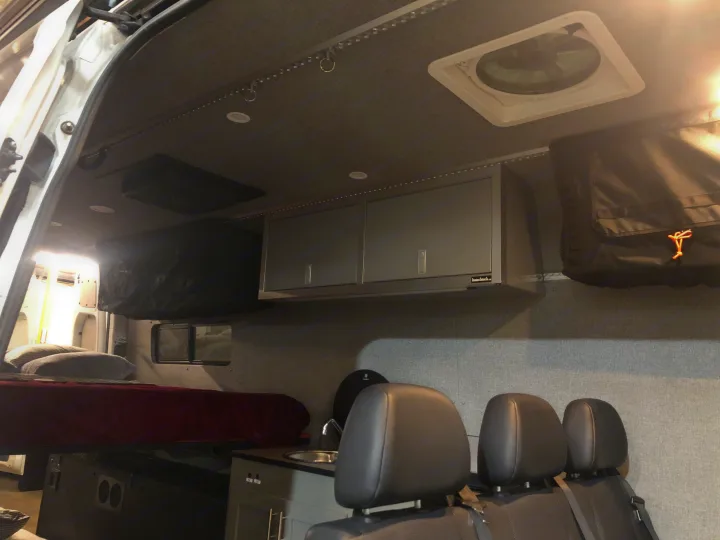 Spacious RV rental interior with a comfortable bed, kitchen area, overhead storage cabinets, and ceiling fan.. Freightliner Sprinter 2012