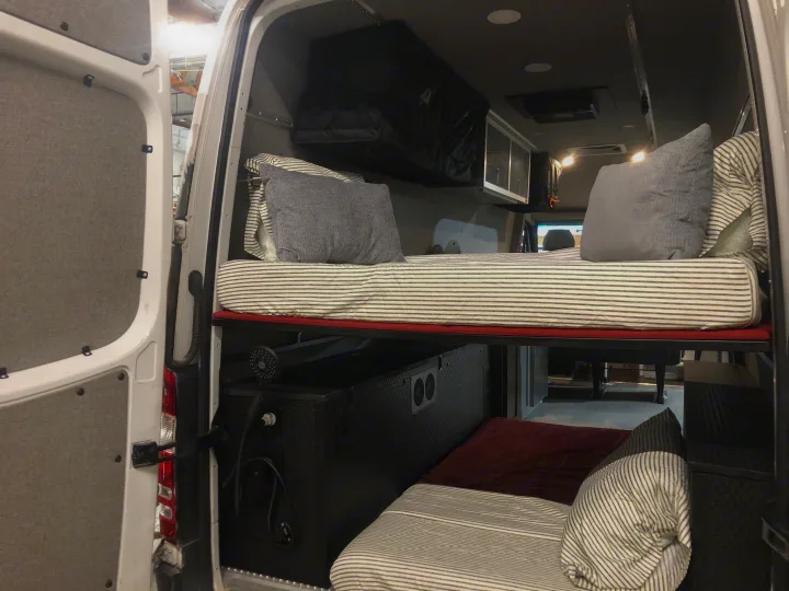 RV rental camper van interior with clever bunk beds, overhead storage, and a built-in shower, optimizing mobile living space.. Freightliner Sprinter 2012