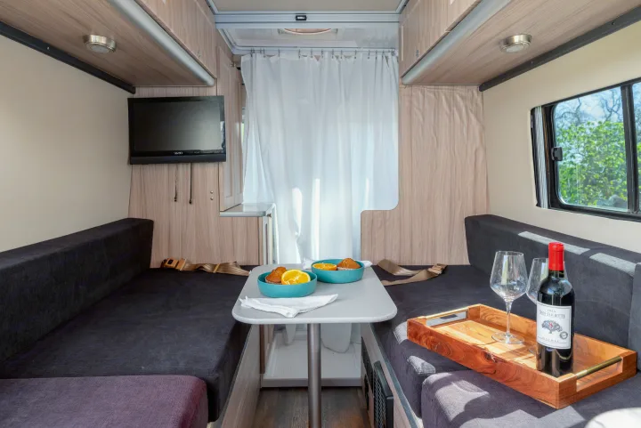 Cozy rv rental interior featuring facing benches, dining table with breakfast, TV, and wine for a comfy camper van experience.. Hymer Sunlight Van 1 2018