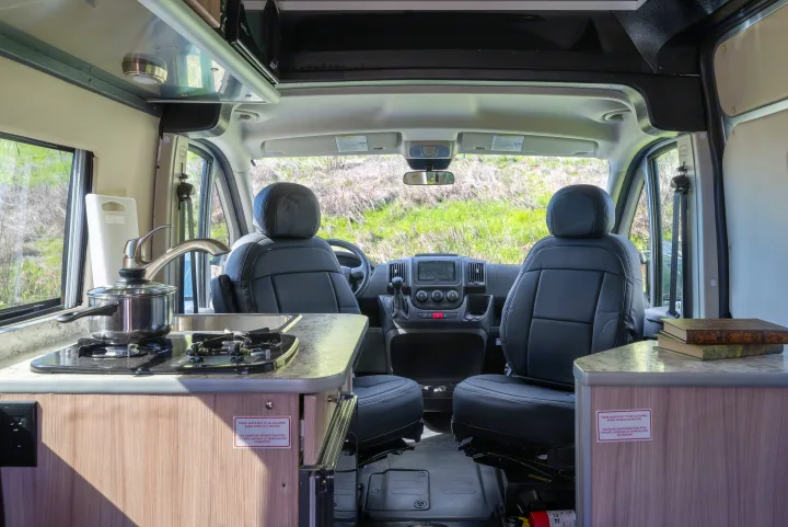 An RV rental interior with a kitchenette (stove, sink), swiveling front seats, and dashboard. Ideal for comfortable road trips.. Hymer Sunlight Van 1 2018