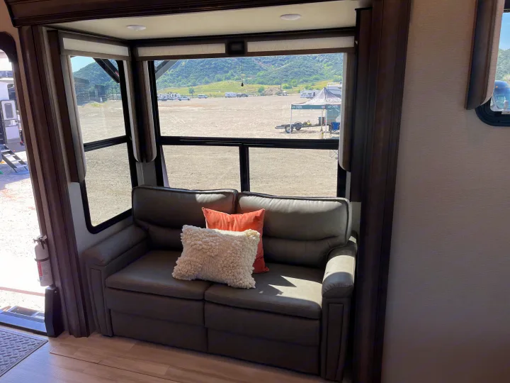 RV rental interior featuring a comfy sofa, decorative pillows, and an expansive view of a sunny outdoor gathering.. Grand Design Solitude 2022