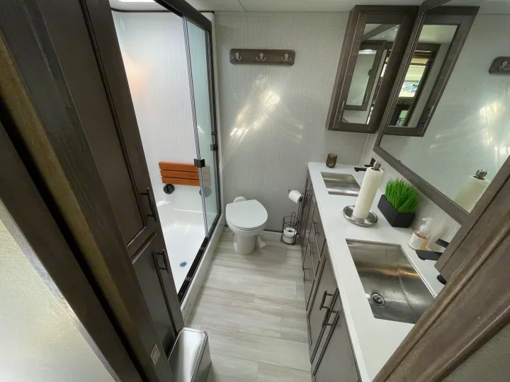 Modern and well-equipped RV bathroom, ideal for your next rv rental trip. Features a shower with a seat, toilet, and dual sinks.. Grand Design Solitude 2022