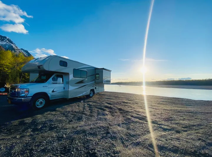 This RV rental offers stunning views! A light-colored motorhome is parked on a rocky riverbank, mountains behind.. Winnebago Minnie Winnie 2020