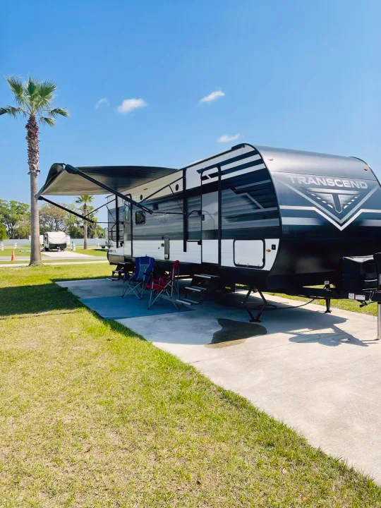 Enjoy a sunny campsite with this spacious rv rental, featuring a deployed awning and chairs under a palm tree.. Grand Design 265BH 2023