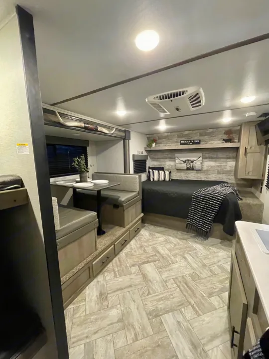 RV rental interior: A cozy, rustic-themed living space with a black bed, dining booth, and light flooring. Longhorn decor visible.. Keystone Springdale 2021