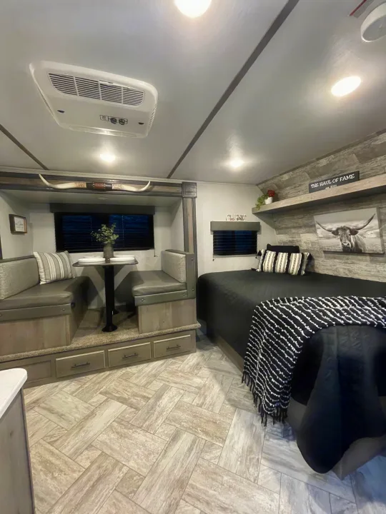 This rv rental shows a cozy bedroom with bed, and dining nook with benches. Rustic decor & herringbone floors blend for comfort.. Keystone Springdale 2021