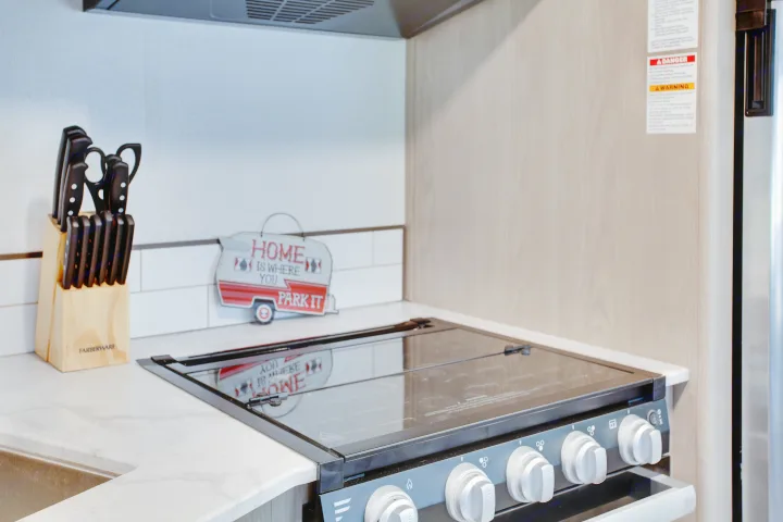 A cozy RV rental kitchen featuring a compact stove, sink, knife block, and a "Home is Where You Park It" sign.. Cruiser Rv Corp Shadow Cruiser 2021