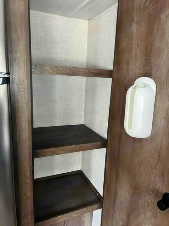 This RV rental features a practical interior storage cabinet with two dark wooden shelves, ideal for pantry or linen storage.. Forest River Wildwood X-Lite 2020