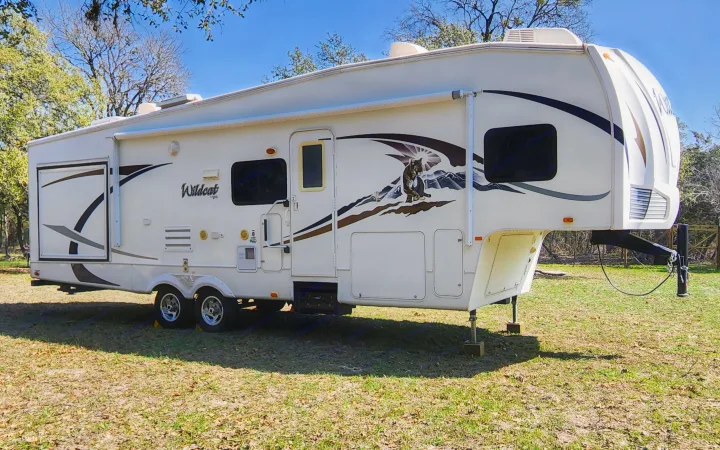 A large white fifth-wheel RV rental is parked on a sunny, grassy lot, ready for adventure.. Forest River Wildcat 2008